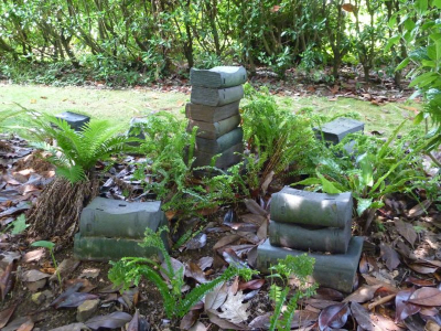 Escultura de Caxigueiro consistente en varias pilas de libros de cerámica escura. Están colocados no xardín arrodeados de fentos